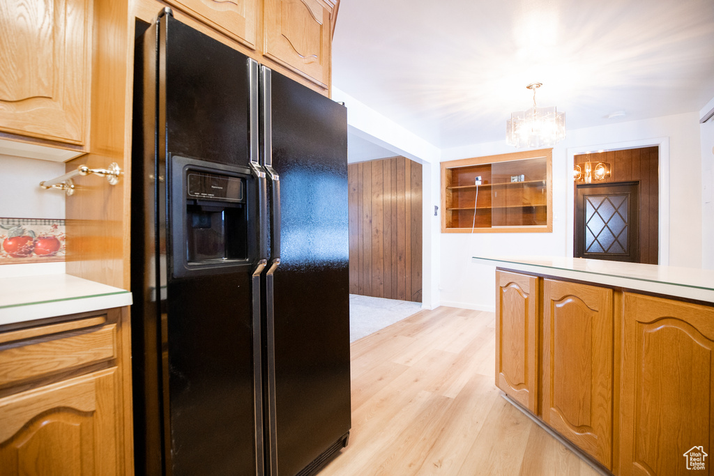 Kitchen with pendant lighting, light hardwood / wood-style floors, black fridge with ice dispenser, and a notable chandelier