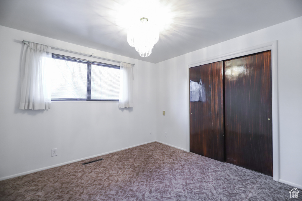 Unfurnished bedroom featuring carpet flooring, a closet, and a notable chandelier