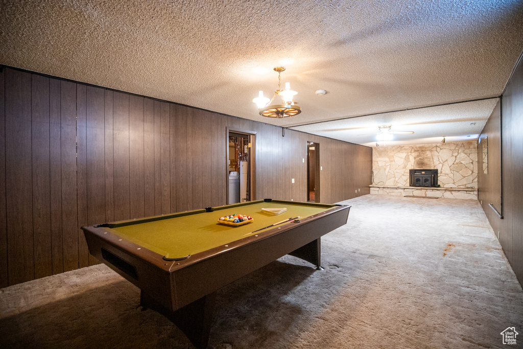 Recreation room featuring wooden walls, a stone fireplace, billiards, and a textured ceiling