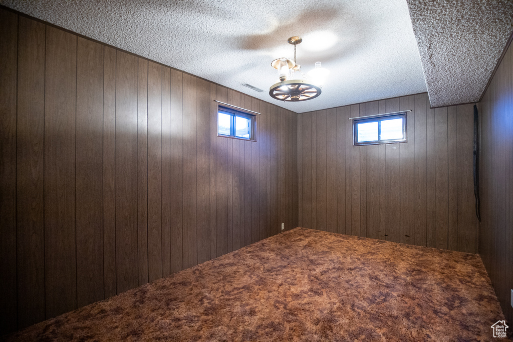 Empty room featuring an inviting chandelier, wooden walls, and carpet