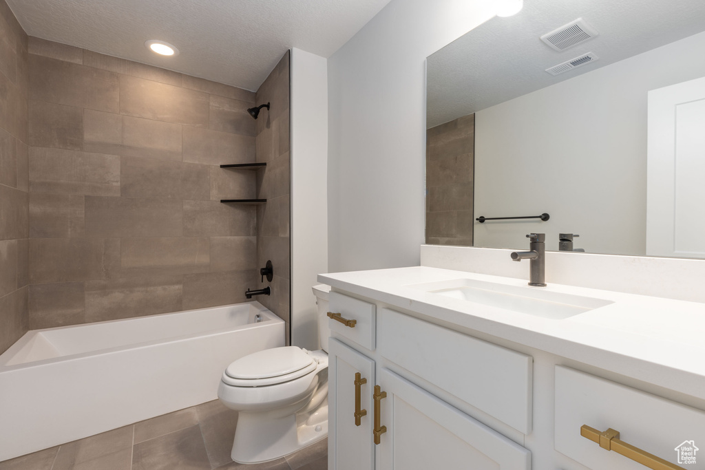 Full bathroom featuring oversized vanity, toilet, tile flooring, and tiled shower / bath combo
