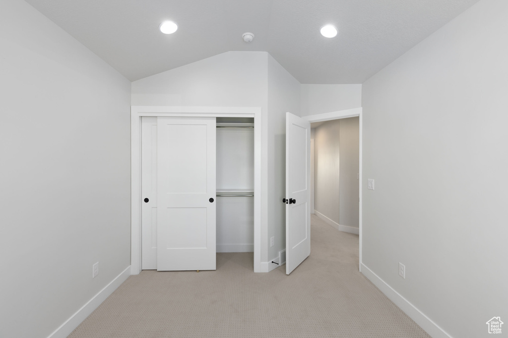 Unfurnished bedroom with a closet, lofted ceiling, and light colored carpet
