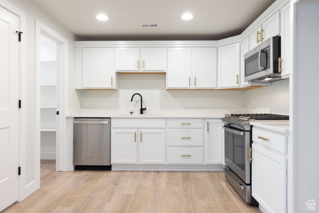 Kitchen featuring light hardwood / wood-style flooring, white cabinets, appliances with stainless steel finishes, and sink
