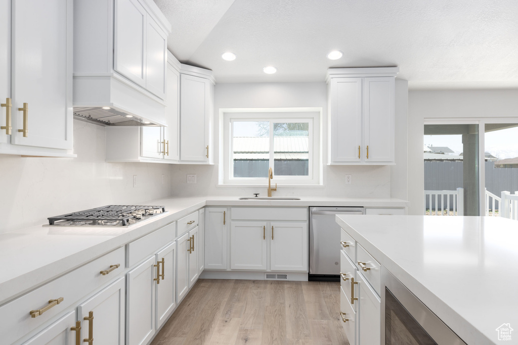 Kitchen with white cabinets, light wood-type flooring, sink, and stainless steel appliances