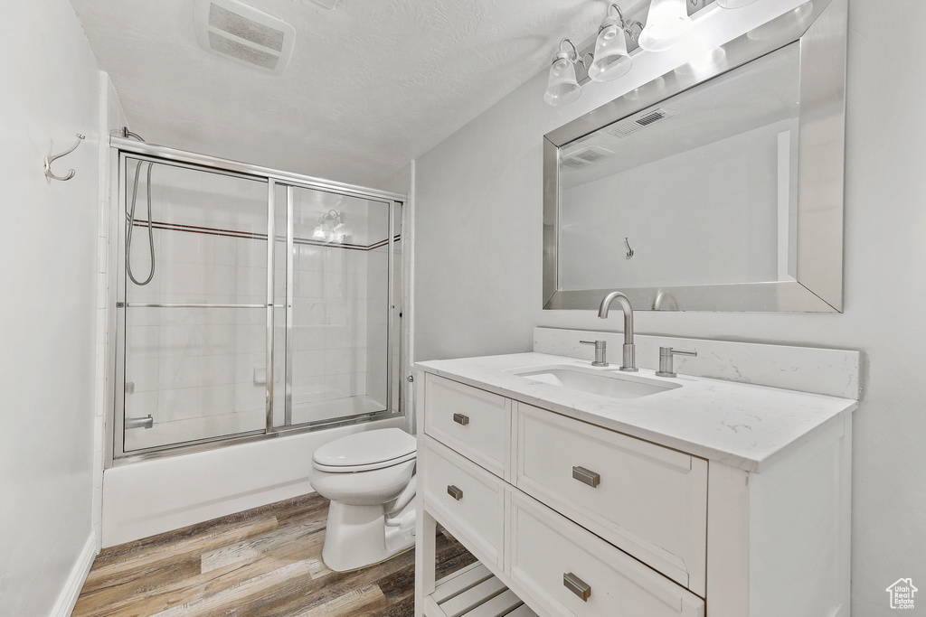 Full bathroom with wood-type flooring, toilet, vanity, and bath / shower combo with glass door