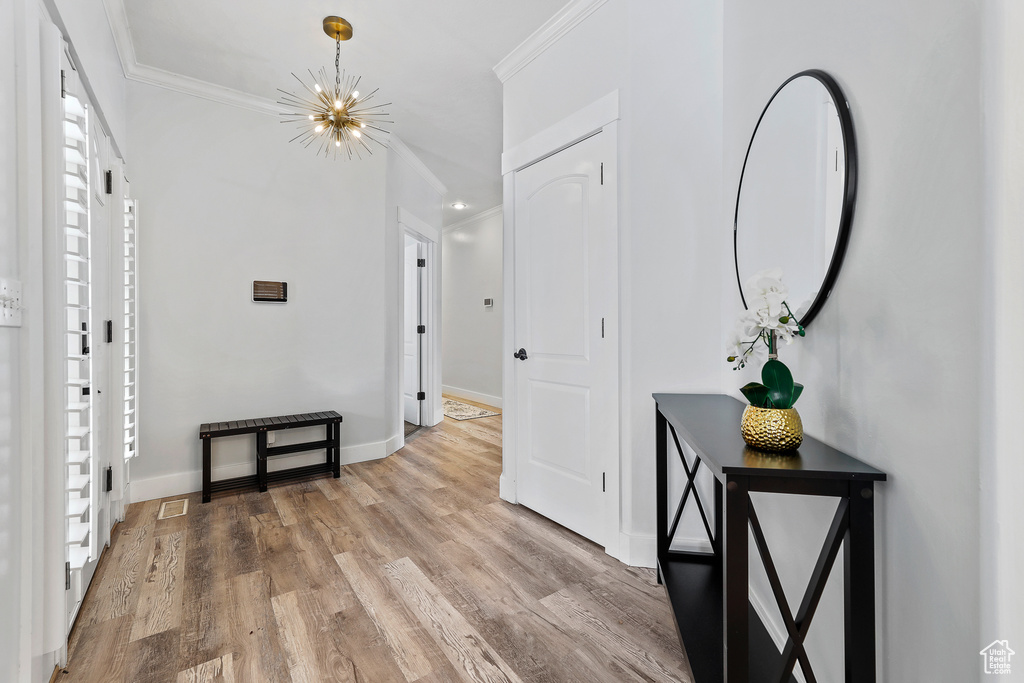 Corridor featuring an inviting chandelier, light hardwood / wood-style flooring, and ornamental molding