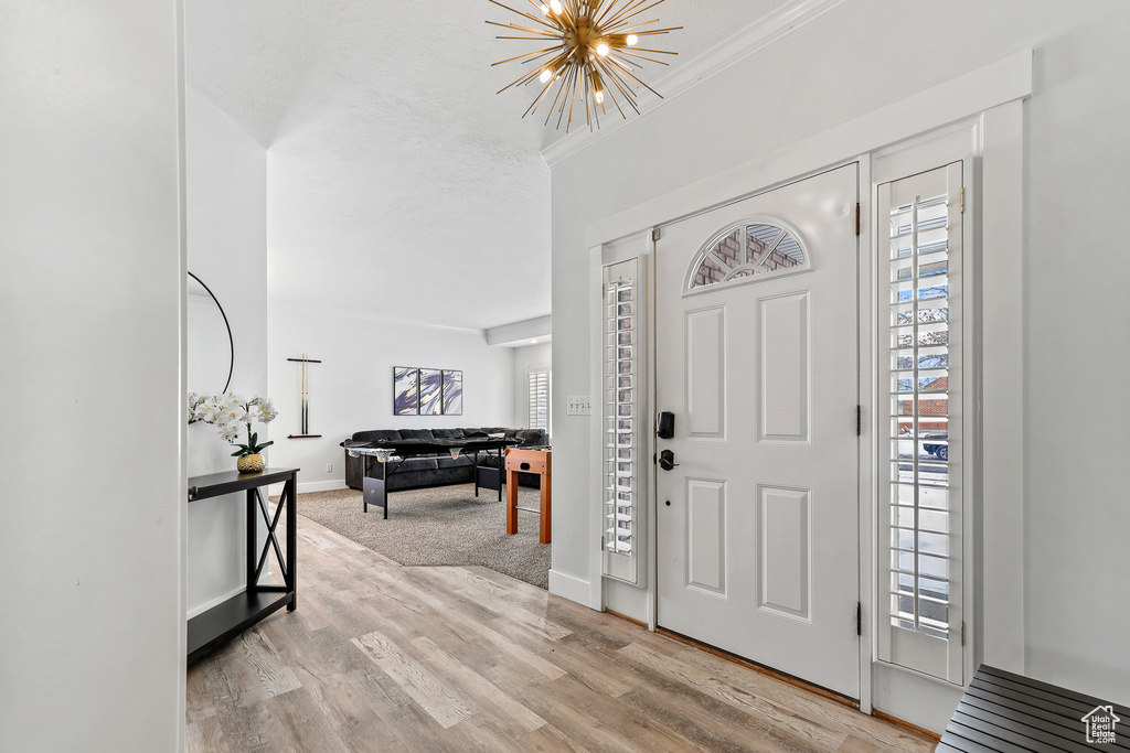 Entrance foyer with crown molding, light hardwood / wood-style floors, and a notable chandelier