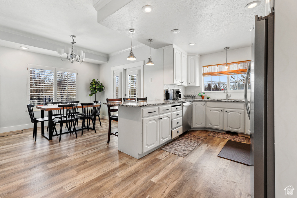Kitchen with an inviting chandelier, white cabinetry, decorative light fixtures, appliances with stainless steel finishes, and light hardwood / wood-style flooring