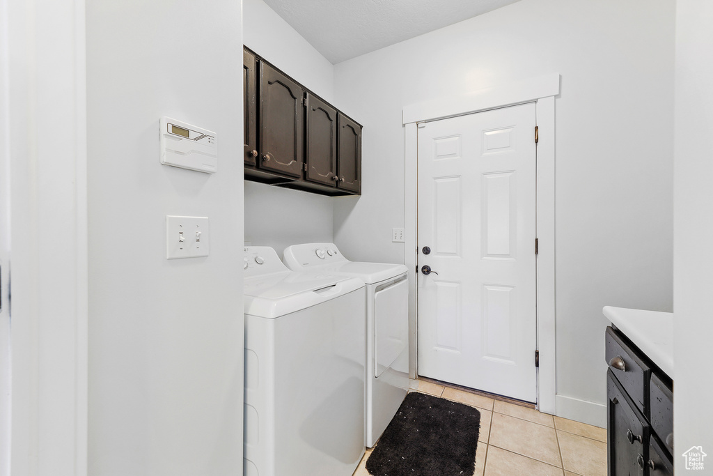 Washroom with light tile flooring, cabinets, and washing machine and dryer