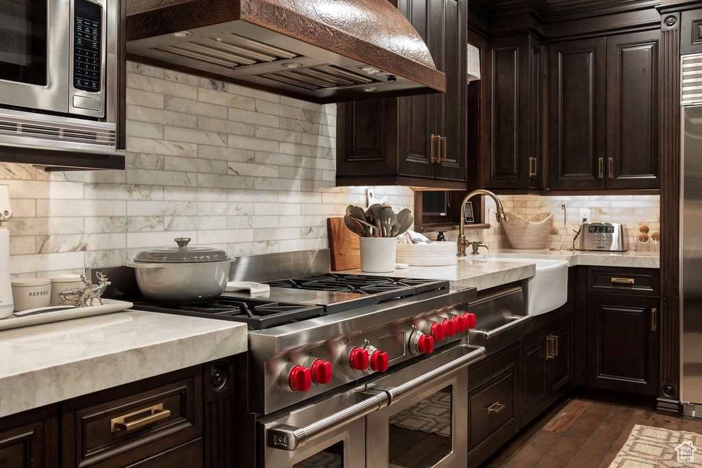 Kitchen featuring custom range hood, stainless steel appliances, dark hardwood / wood-style floors, decorative backsplash, and dark brown cabinetry