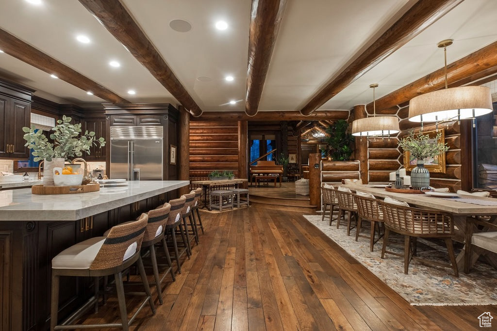 Dining space featuring dark wood-type flooring, rustic walls, sink, and beamed ceiling