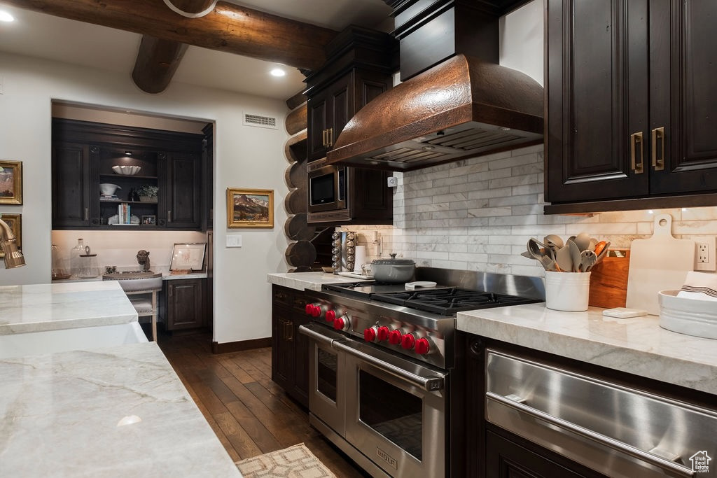 Kitchen with double oven range, light stone counters, backsplash, dark hardwood / wood-style floors, and wall chimney range hood