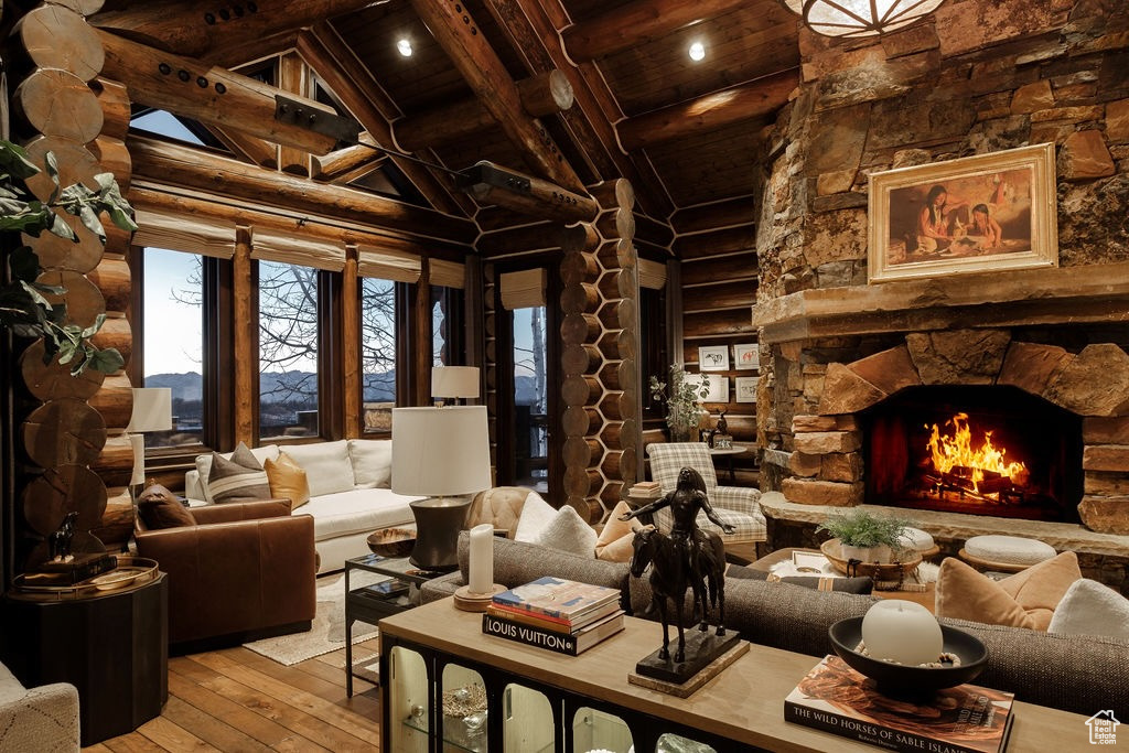 Living room featuring a fireplace, beam ceiling, rustic walls, light wood-type flooring, and high vaulted ceiling