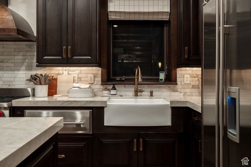 Kitchen with sink, high end refrigerator, decorative backsplash, and wall chimney range hood