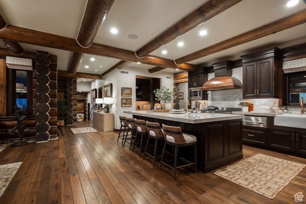 Kitchen featuring dark hardwood / wood-style flooring, a breakfast bar area, custom exhaust hood, backsplash, and a center island with sink