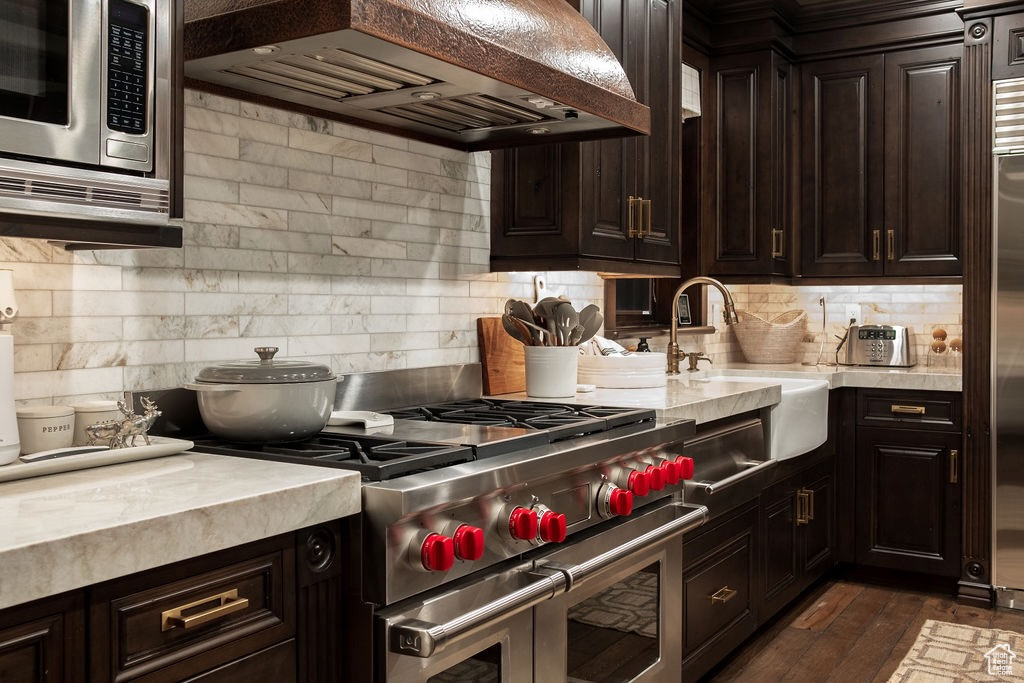 Kitchen featuring dark hardwood / wood-style flooring, dark brown cabinetry, appliances with stainless steel finishes, custom range hood, and tasteful backsplash