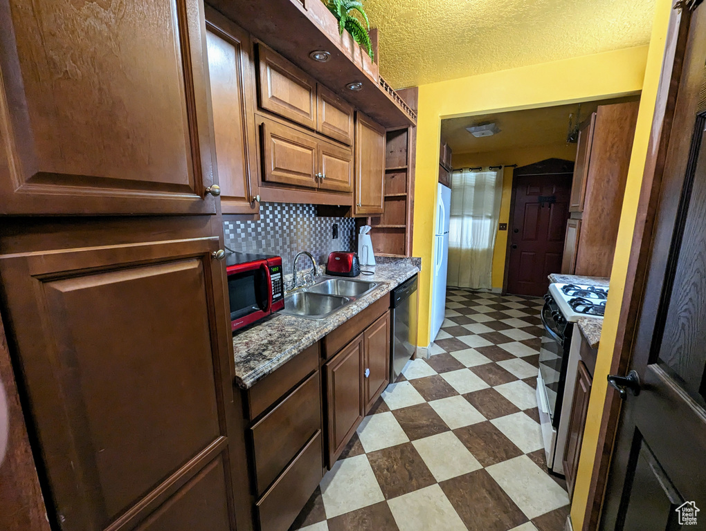 Kitchen featuring stainless steel appliances, dark tile flooring, tasteful backsplash, sink, and a textured ceiling