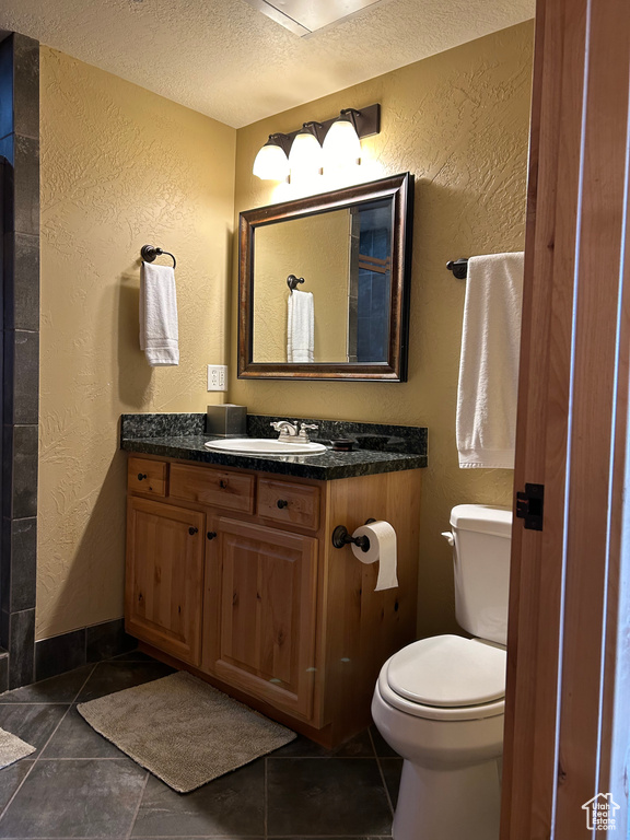 Bathroom with oversized vanity, toilet, a textured ceiling, and tile floors