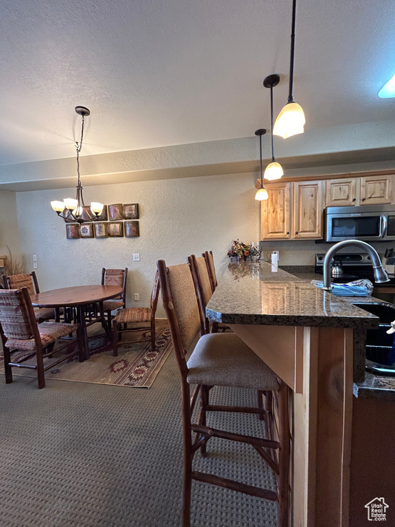Kitchen featuring dark colored carpet, kitchen peninsula, a kitchen breakfast bar, a chandelier, and pendant lighting