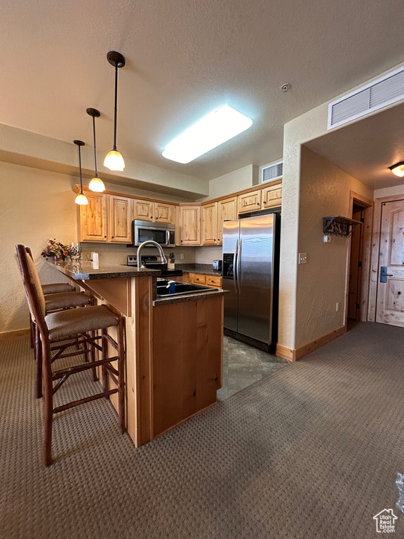 Kitchen featuring hanging light fixtures, a breakfast bar area, stainless steel appliances, kitchen peninsula, and dark carpet
