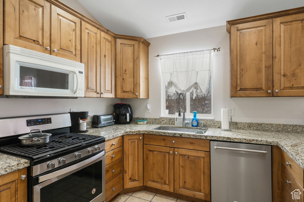 Kitchen with sink, light stone countertops, appliances with stainless steel finishes, and light tile floors