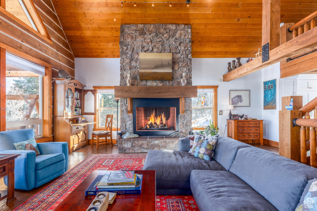 Living room featuring dark wood-type flooring, a stone fireplace, high vaulted ceiling, and wood ceiling