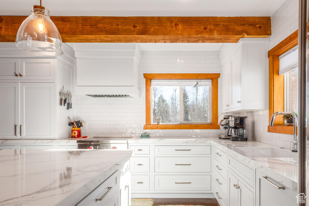 Kitchen with pendant lighting, tasteful backsplash, light stone countertops, white cabinets, and sink