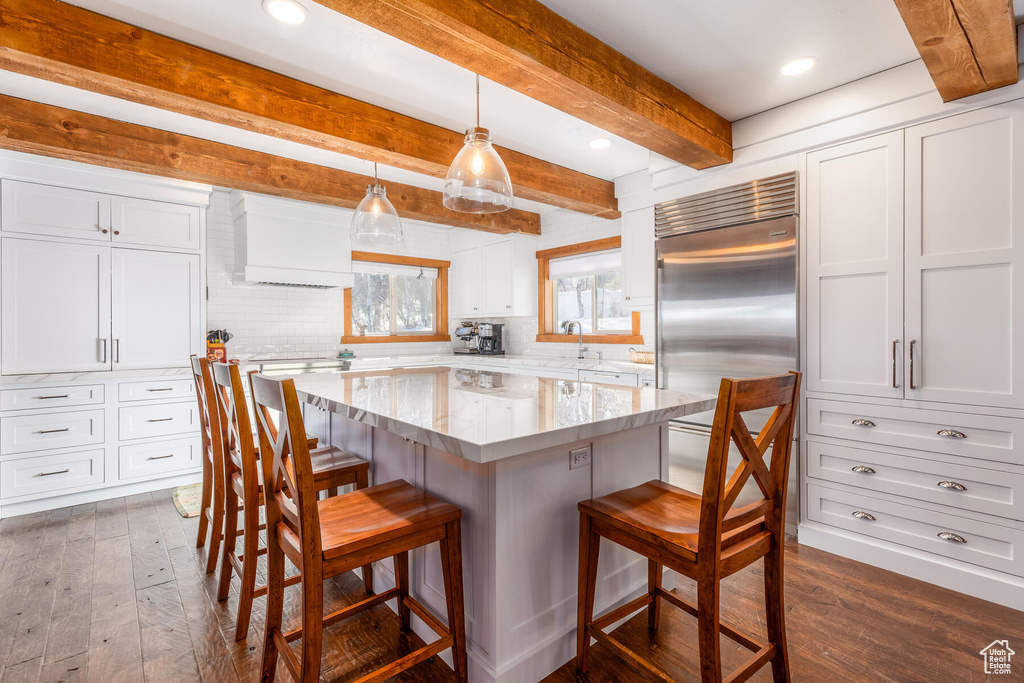 Kitchen featuring built in refrigerator, a kitchen breakfast bar, pendant lighting, dark wood-type flooring, and white cabinets