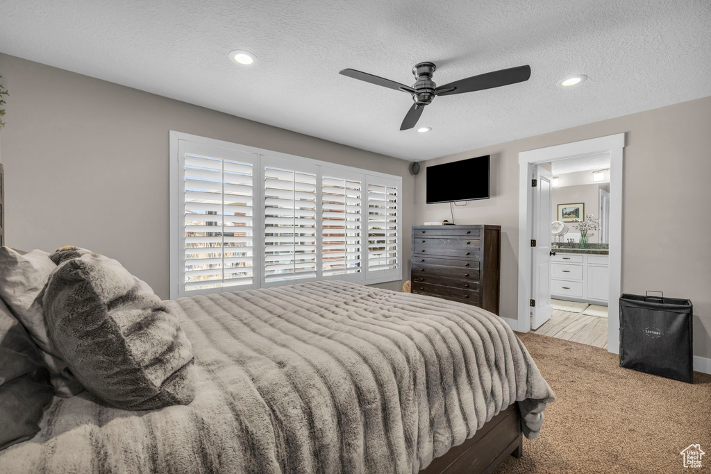 Bedroom featuring ensuite bathroom, a textured ceiling, light colored carpet, and ceiling fan