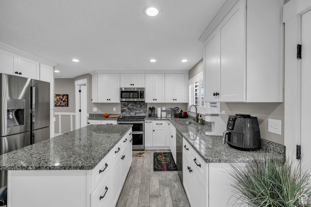 Kitchen featuring white cabinets, a center island, light hardwood / wood-style flooring, stainless steel appliances, and sink