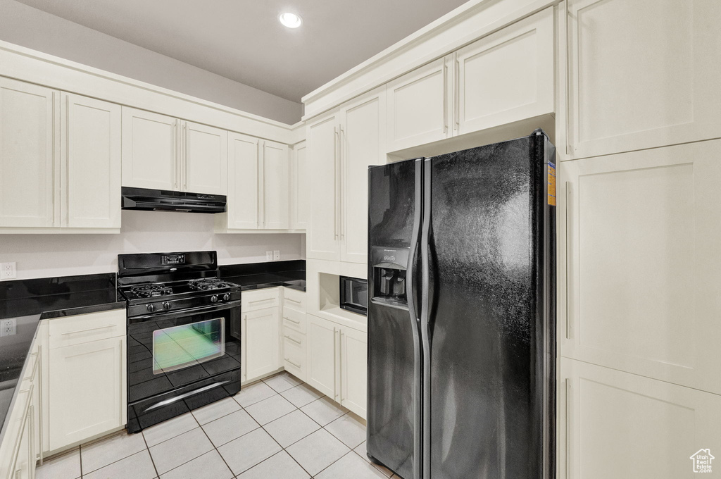 Kitchen featuring white cabinets, light tile floors, black appliances, and dark stone countertops