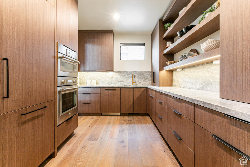 Kitchen with double oven, light stone counters, backsplash, sink, and light wood-type flooring