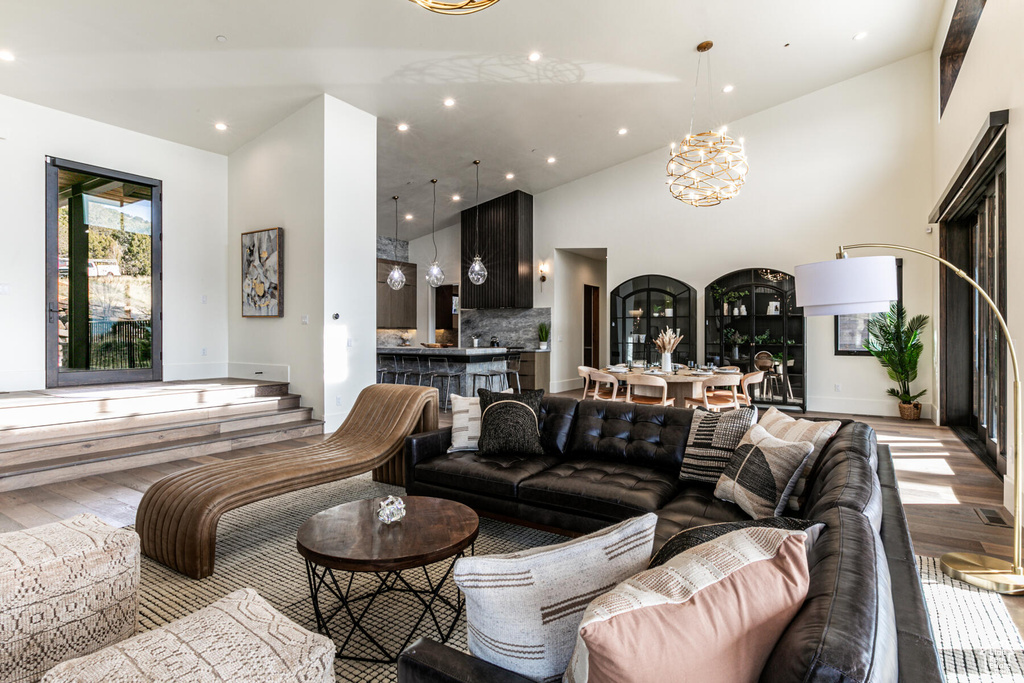 Living room with light wood-type flooring, an inviting chandelier, and high vaulted ceiling