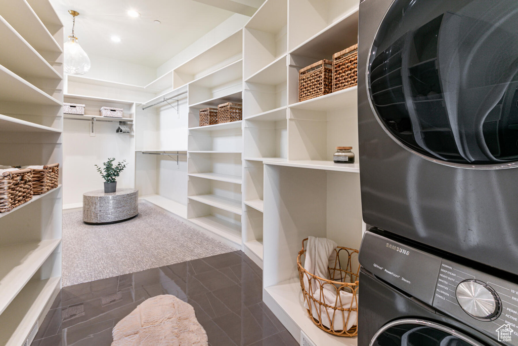 Walk in closet with dark carpet and stacked washer and clothes dryer