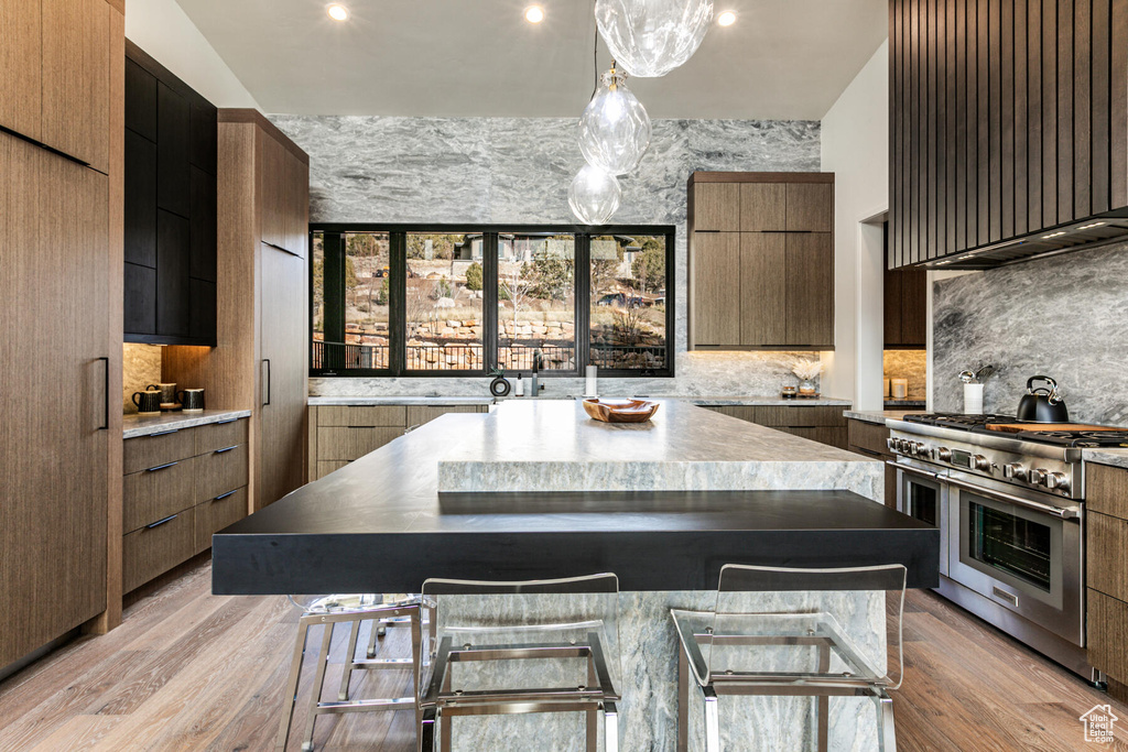 Kitchen with decorative light fixtures, a breakfast bar area, wall chimney exhaust hood, light hardwood / wood-style flooring, and double oven range