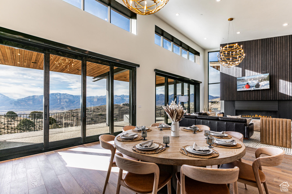 Dining area with an inviting chandelier, a mountain view, a high ceiling, hardwood / wood-style flooring, and a fireplace