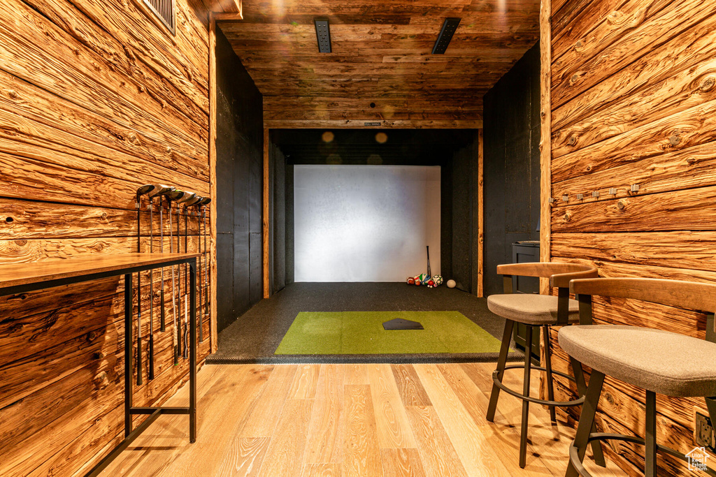 Game room with light hardwood / wood-style flooring, golf simulator, bar area, and wood ceiling