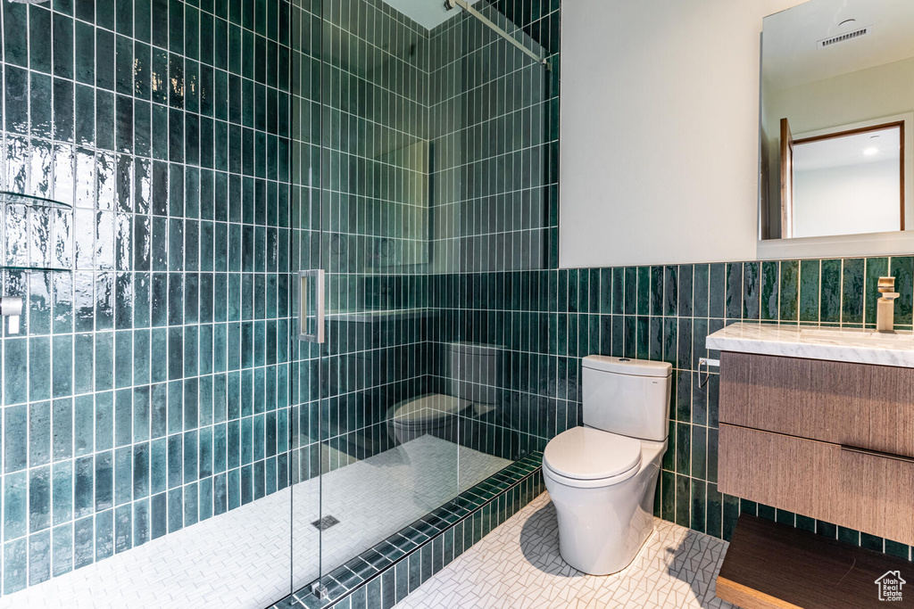 Bathroom with tile walls, vanity, toilet, and a tile shower