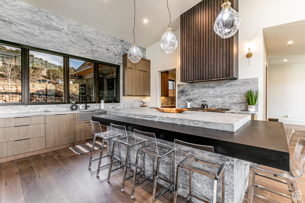 Kitchen with tasteful backsplash, a kitchen breakfast bar, decorative light fixtures, and dark wood-type flooring