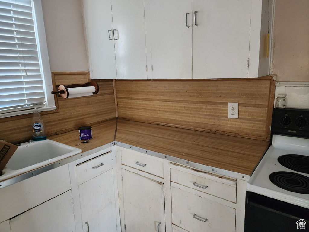 Kitchen with white electric range oven, white cabinets, sink, and tasteful backsplash