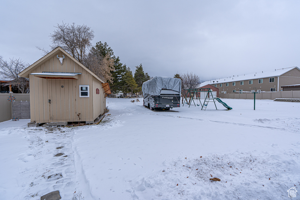 Yard covered in snow with a storage unit and a playground