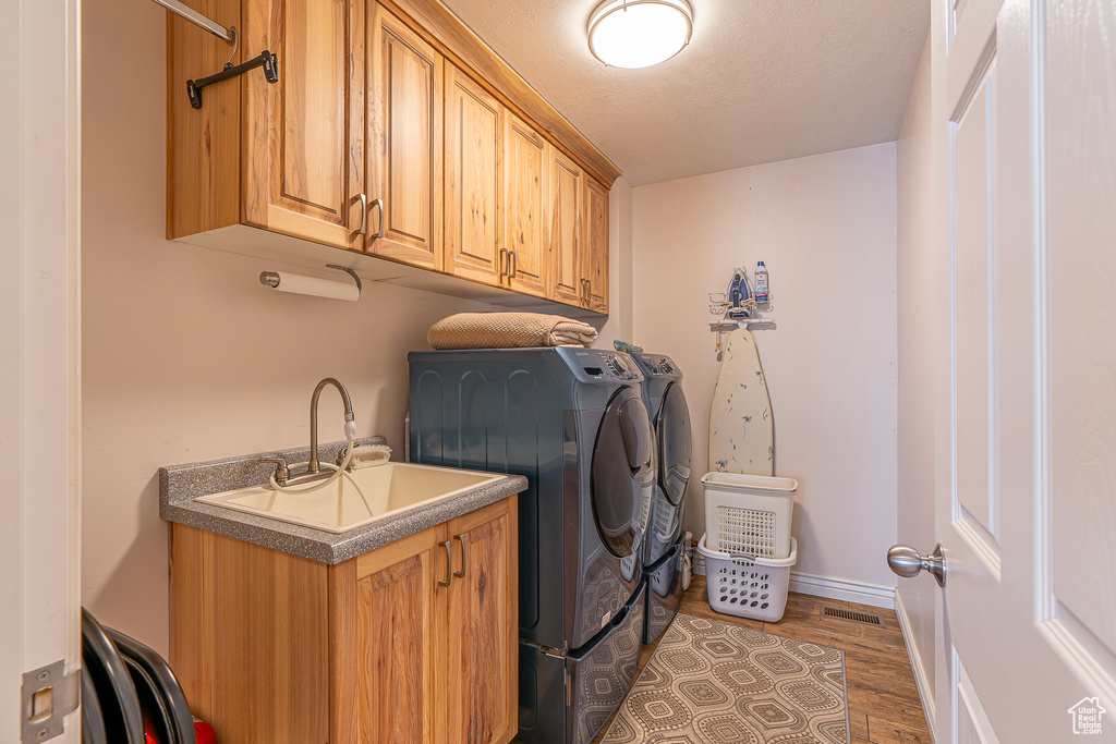 Laundry room with washing machine and dryer, cabinets, sink, and dark hardwood / wood-style floors