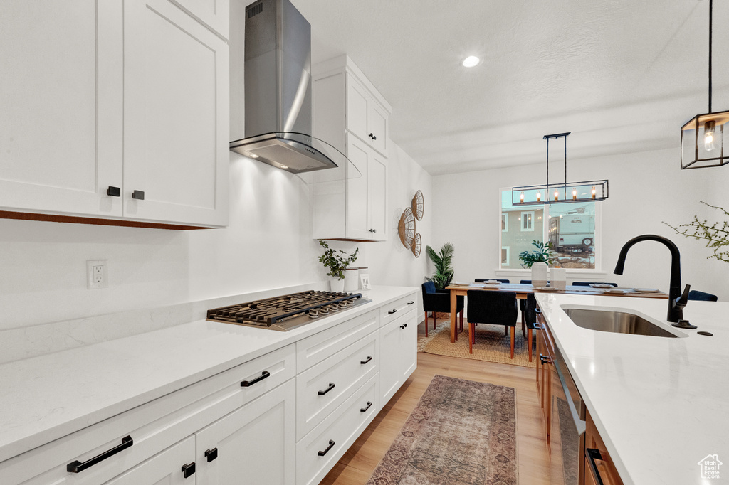 Kitchen featuring wall chimney exhaust hood, white cabinetry, decorative light fixtures, light hardwood / wood-style flooring, and sink
