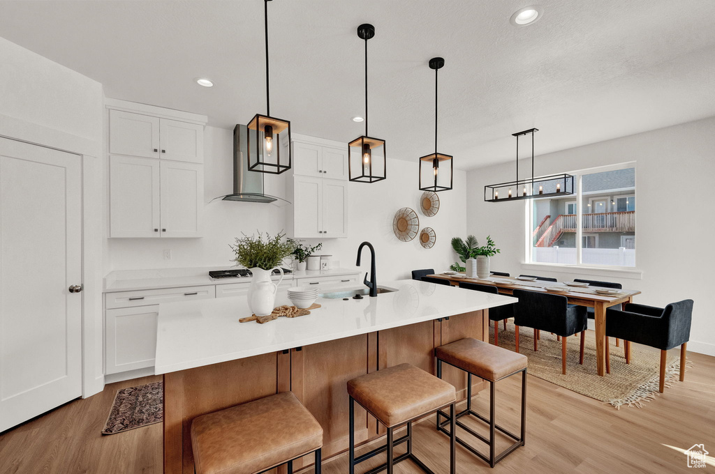 Kitchen with white cabinetry, sink, wall chimney range hood, pendant lighting, and light wood-type flooring