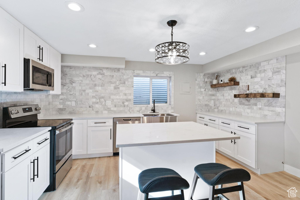 Kitchen with an inviting chandelier, light hardwood / wood-style floors, white cabinets, pendant lighting, and stainless steel appliances