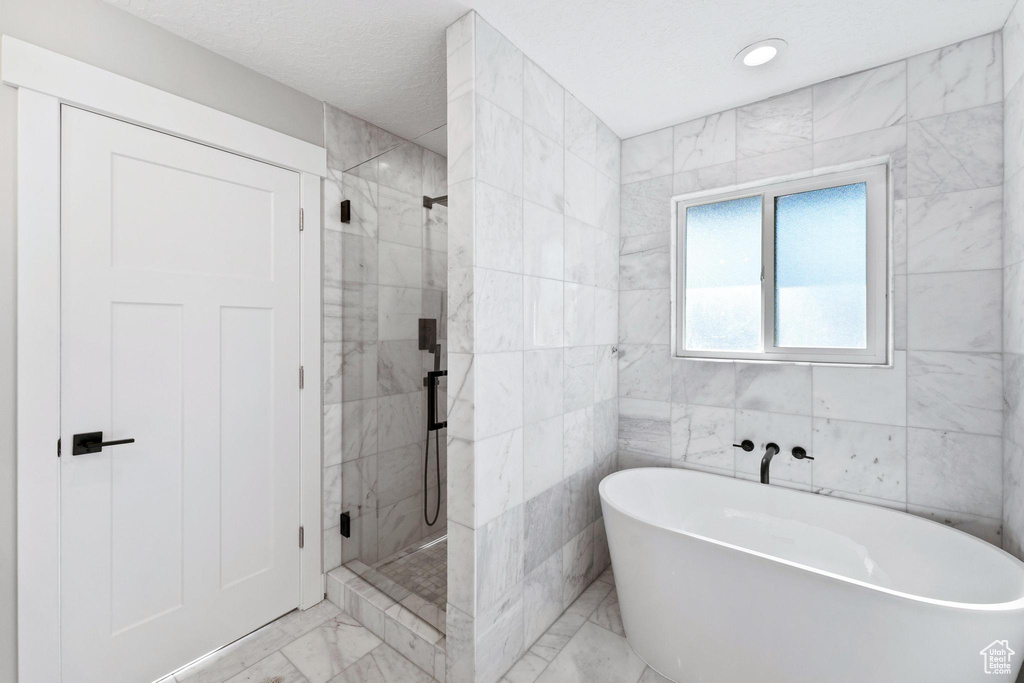 Bathroom with tile floors, tile walls, and separate shower and tub