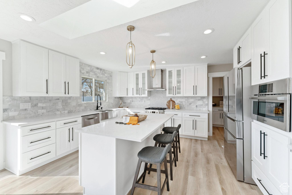 Kitchen featuring a kitchen bar, white cabinets, light hardwood / wood-style flooring, stainless steel appliances, and a kitchen island