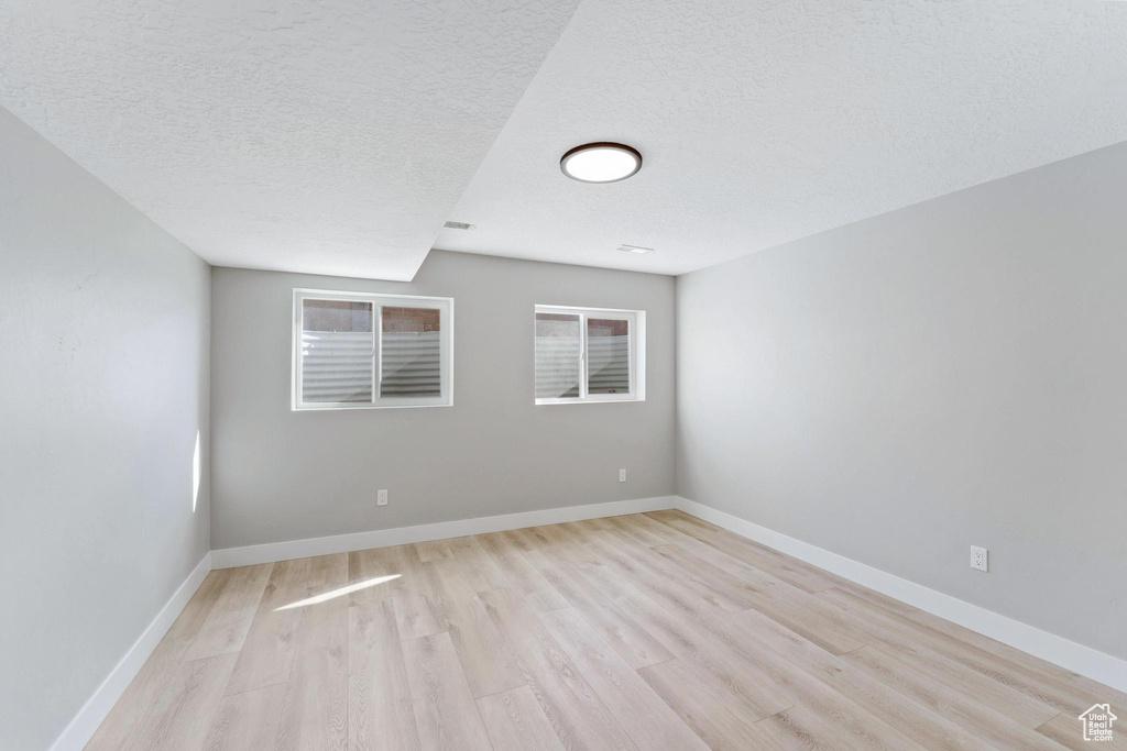 Empty room with light hardwood / wood-style floors and a textured ceiling