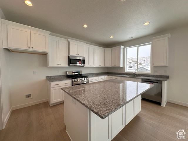 Kitchen featuring white cabinets, appliances with stainless steel finishes, a center island, and light hardwood / wood-style flooring
