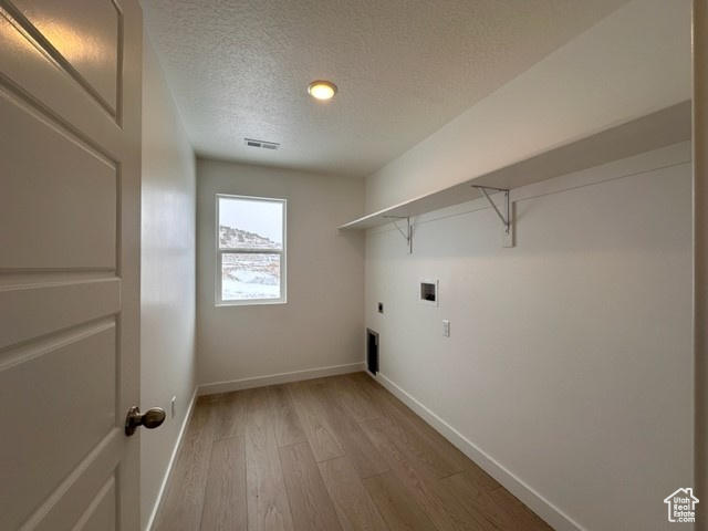 Washroom with electric dryer hookup, light hardwood / wood-style floors, a textured ceiling, and washer hookup